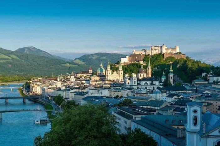 Blick über Salzburg mit Festung Hohensalzburg, Altstadt und umliegende Berge bei Sonnenschein